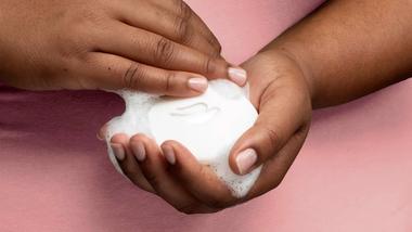 ภาพระยะใกล้ของมือผู้หญิงซึ่งถือสบู่ Dove Beauty Bar ที่มีฟองอยู่