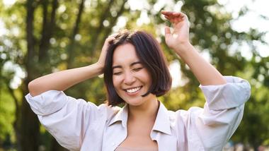 หญิงสาวกำลังยิ้มท่ามกลางธรรมชาติ หลับตา และยกมือขึ้น