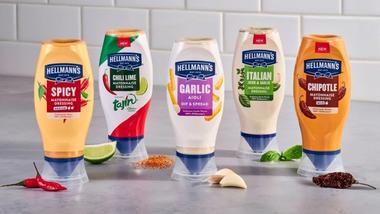 ภาพมายองเนสปรุงรสในขวดบีบของ Hellmann’s พร้อมส่วนผสมหลัก เช่น มะนาว พริก กระเทียม และสมุนไพร